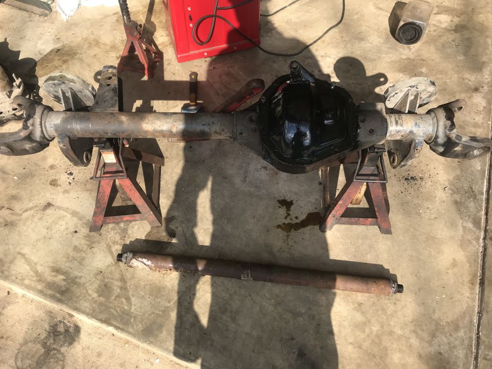 Rear axle assembly with black differential cover on jack stands, driveshaft on ground