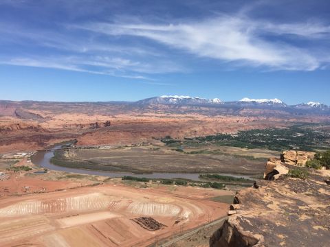 1984 Ford Bronco - A wide panoramic view of a desert landscape with a river winding through it, leading to distant snow-capped mountains under a blue sky with…
