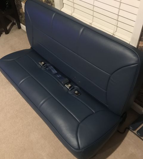 1995 Ford Bronco - A navy blue bench seat with integrated seat belts is shown from a high angle, resting on a carpeted floor. The seat appears to be from a ve…
