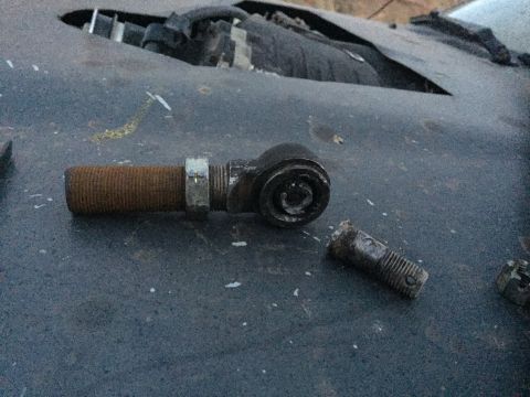 1984 Ford Bronco - A rusty tie rod end and a broken bolt lie on a dark, textured surface, possibly a vehicle hood.