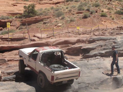 1984 Ford Bronco - A white and red Ford Bronco is navigating a rocky off-road trail. A person wearing a dark shirt and jeans walks on the rocks to the right o…