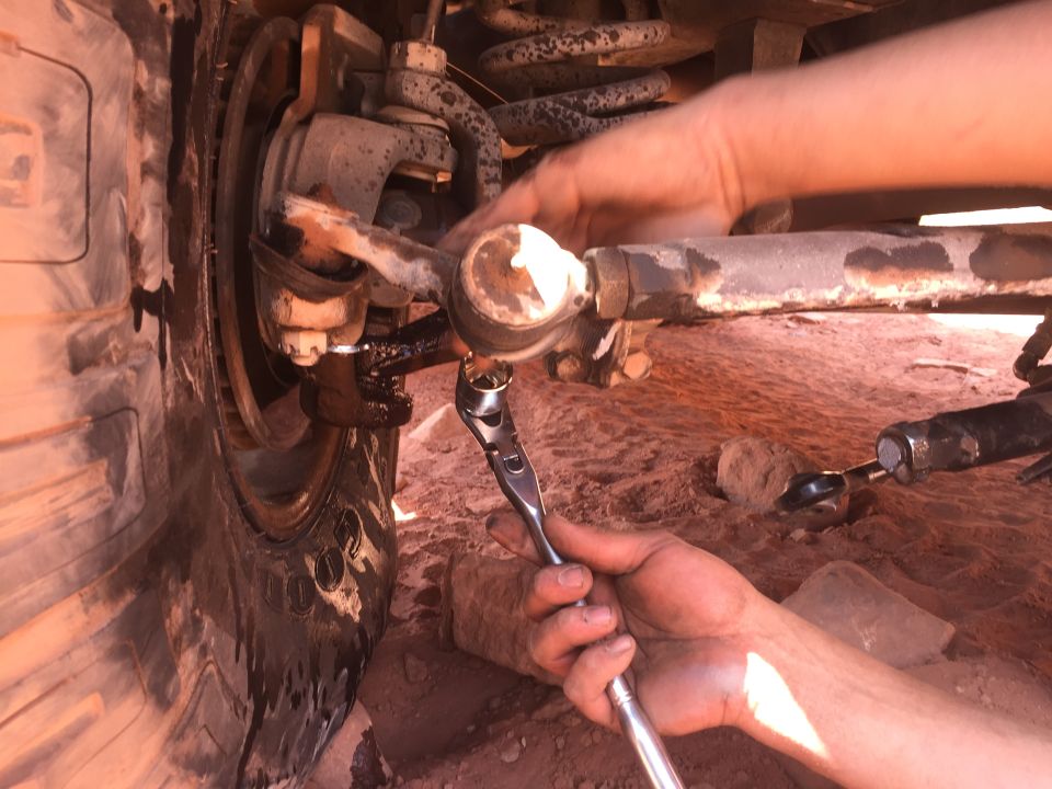 Close-up of a mechanic tightening a tie rod end on a vehicle's front suspension.