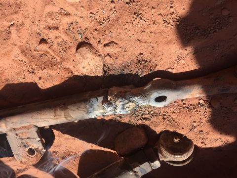 1984 Ford Bronco - A close-up view shows a heavily welded metal rod, likely a suspension component, lying on reddish-brown dirt. Wisps of smoke rise from the…