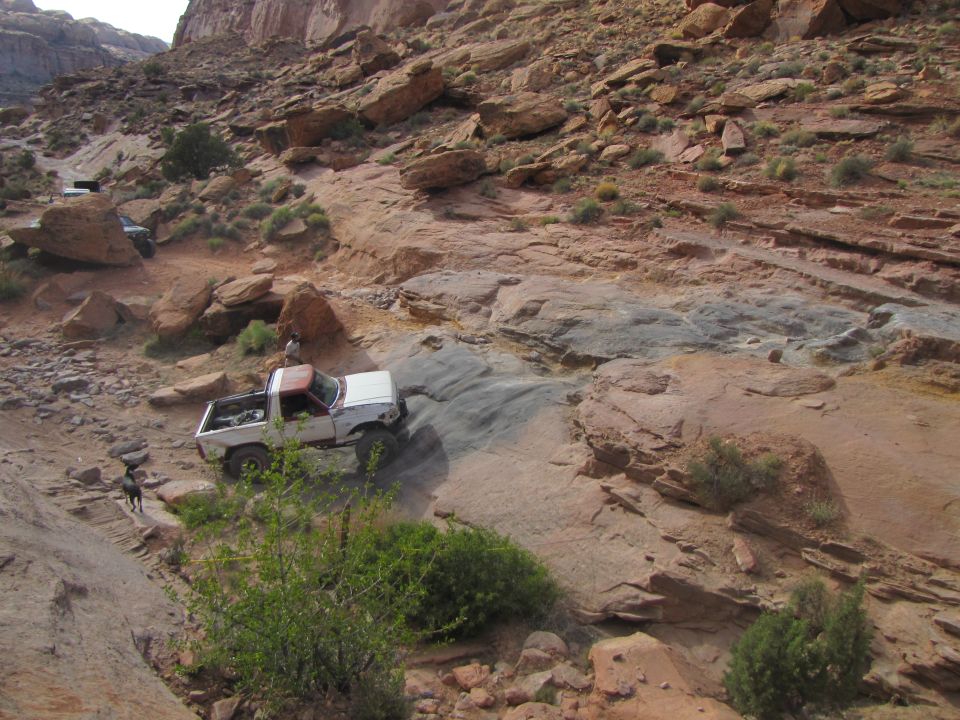 White and red Ford pickup truck driving on a steep, rocky desert trail.