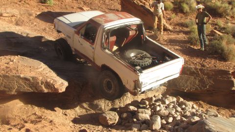 1984 Ford Bronco - A white Ford Bronco is navigating a rocky, off-road trail with two people standing nearby watching. The vehicle is tilted significantly as…
