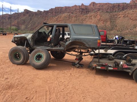 1984 Ford Bronco - A heavily modified off-road vehicle, likely a custom build, is parked on sandy terrain with its front wheels removed and placed beside it.…