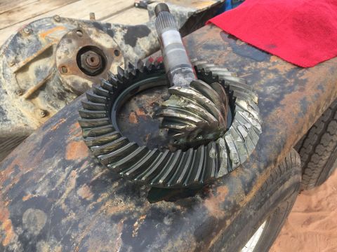 1984 Ford Bronco - A set of differential gears, a pinion shaft, and a differential housing are laid out on a rusty surface. A red cloth is visible in the uppe…