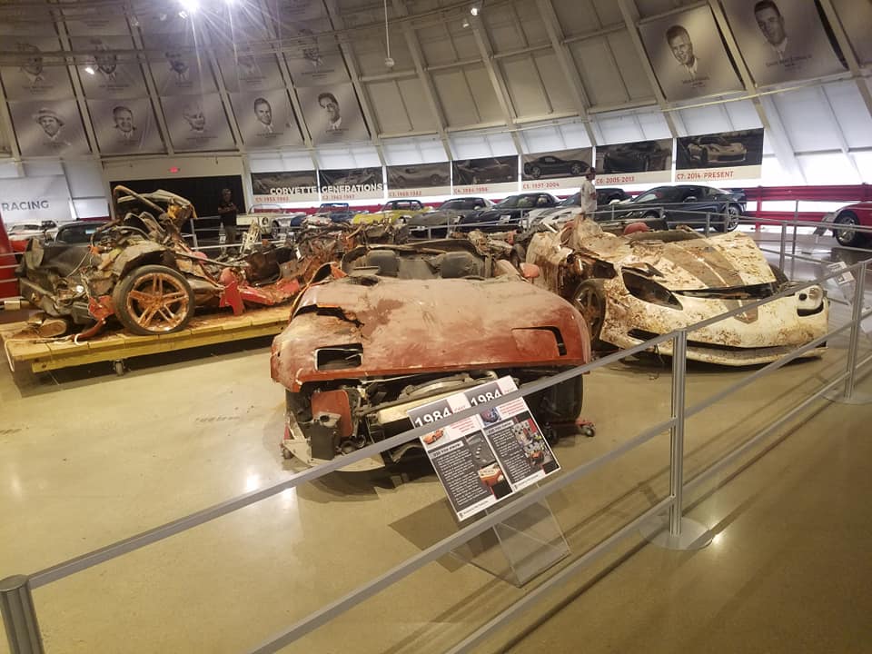 Two wrecked Chevrolet Corvettes, one red and one white, displayed in a museum.