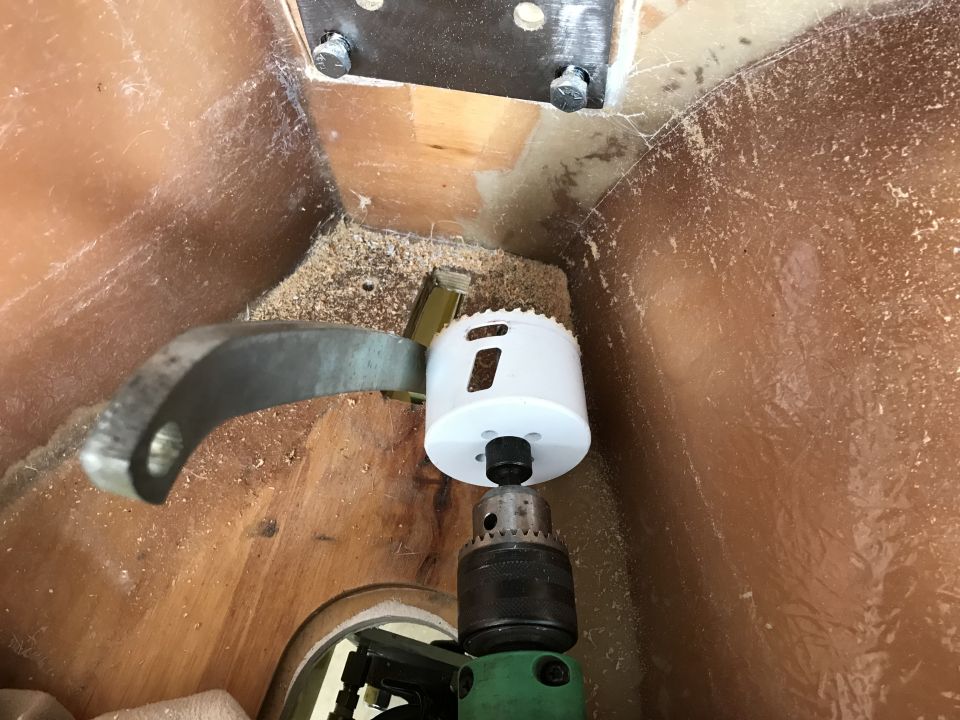 Hole saw attached to a drill cutting into wood, with a metal bracket above.