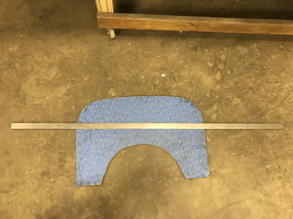 Metal ruler across blue patterned car part on concrete floor