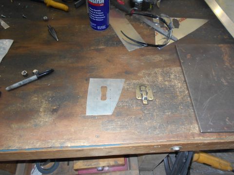 1992 Ford Bronco - A workbench surface with various tools and materials, including a marker, nuts, a metal template with a keyhole shape, and a brass latch.