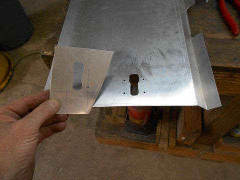 1992 Ford Bronco - A hand holds a piece of sheet metal with a keyhole-shaped cutout and scribe marks. It is being held over a larger piece of sheet metal with…