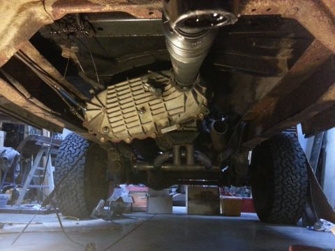 1978 Ford Bronco - The underside of a vehicle shows the transmission, driveshaft, and exhaust system, with large off-road tires visible on either side. The fr…
