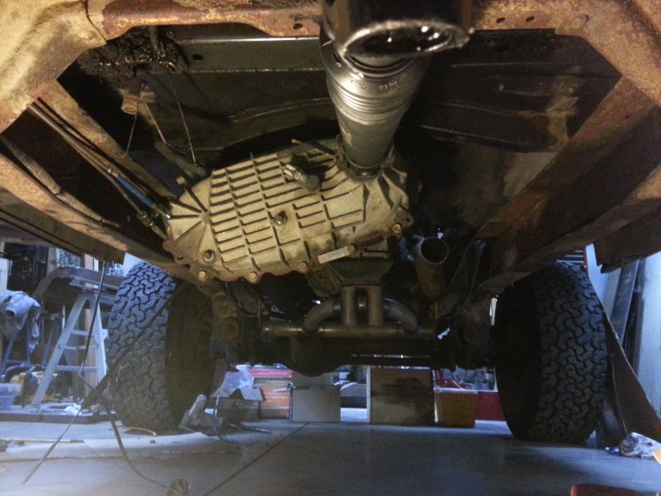 Underside of a vehicle showing transmission, driveshaft, exhaust, and tires.