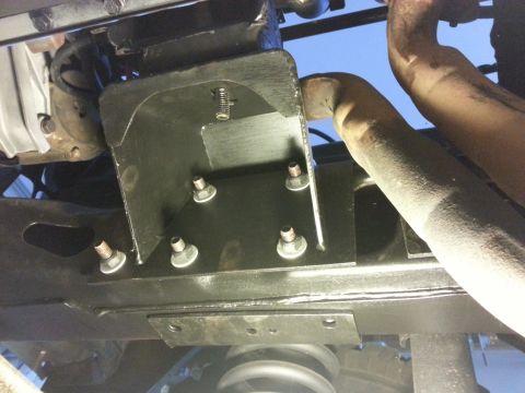 1978 Ford Bronco - This is an underside view of a vehicle's frame, showing a black metal bracket with multiple bolts and a section of exhaust pipe. The bracke…