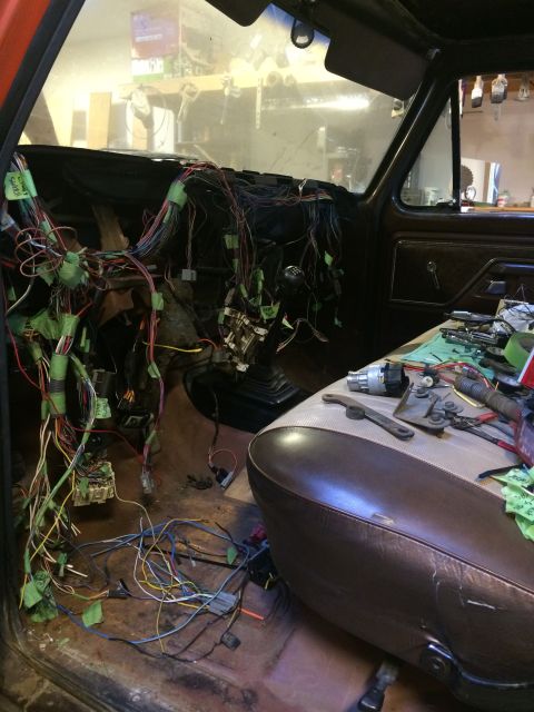 1978 Ford Bronco - The interior of a classic Ford Bronco is shown with the dashboard removed, revealing a complex wiring harness. Various tools and parts are…