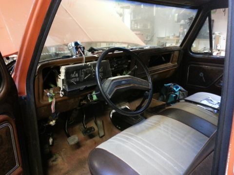 1978 Ford Bronco - The interior of an orange 1978 Ford Bronco is shown with the dashboard partially disassembled. The steering wheel, instrument cluster, and…