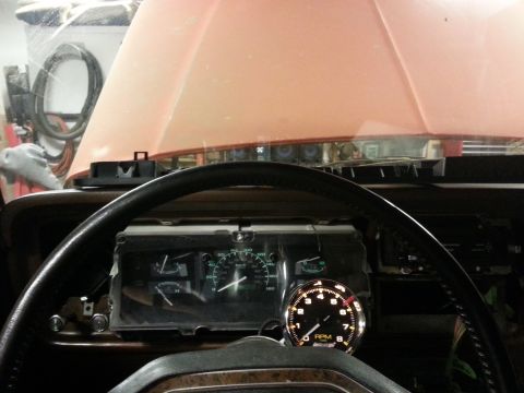 1978 Ford Bronco - Interior view of a vehicle dashboard with the hood open. A steering wheel is in the foreground, with a tachometer and speedometer gauges vi…