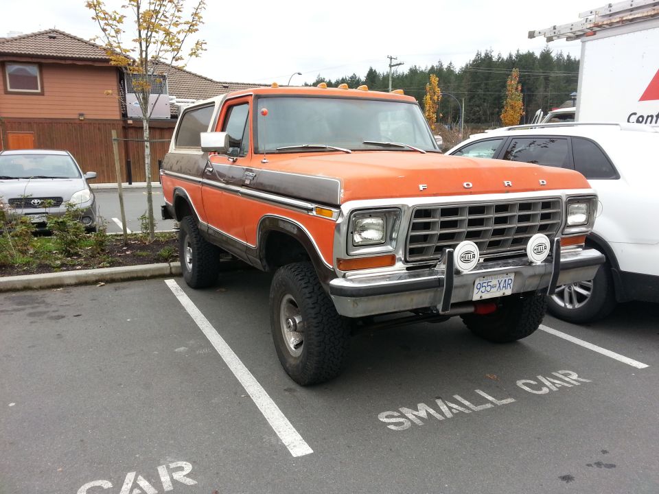 1978 Ford Bronco, orange and brown, lifted, parked in a small car spot.