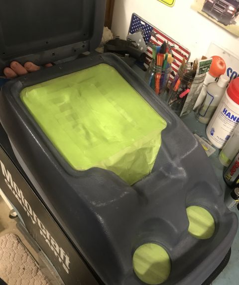 1995 Ford Bronco - A gray plastic center console with green tape covering the storage area and two circular openings. The console is open, revealing a hand in…