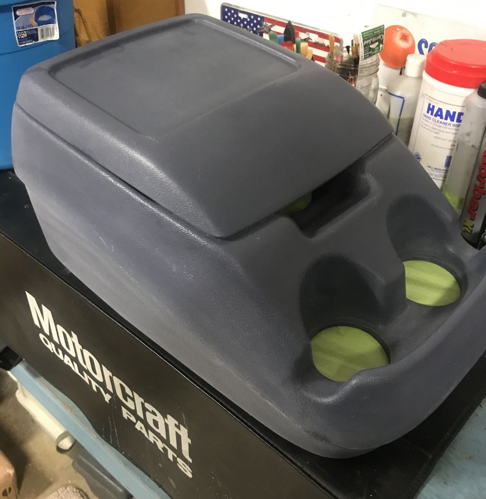 Gray plastic center console with two cup holders on a black box with Motorcraft logo.
