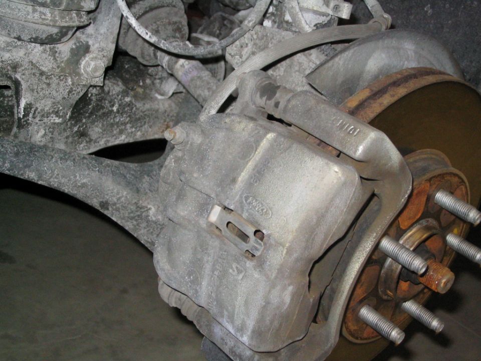 Close-up of a car's front brake caliper and rotor assembly. Ford logo visible on caliper