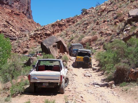 1984 Ford Bronco - A white 1980s Ford Bronco is parked on a rocky, off-road trail, facing away from the camera. Several other off-road vehicles are visible fu…