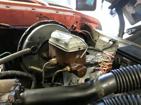 1978 Ford Bronco - The engine bay of a vehicle shows a brake booster and master cylinder assembly with associated wiring and hoses. A black air intake tube is…
