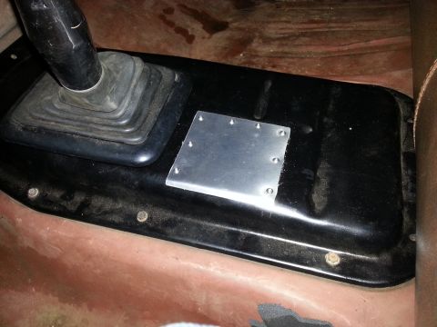 1978 Ford Bronco - A close-up view of the floor console area of a vehicle, showing a black rubber shift boot and a small, bolted-on aluminum plate.