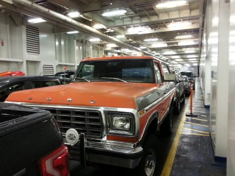 1978 Ford Bronco - A line of vehicles, including an orange and silver Ford pickup truck, are parked on a ferry deck. The truck is in the foreground, showing i…