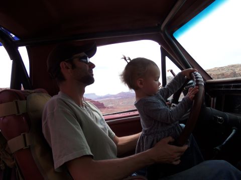 1984 Ford Bronco - A man wearing a baseball cap and sunglasses sits in the driver's seat of a vehicle, while a young child holds the steering wheel. The vehic…
