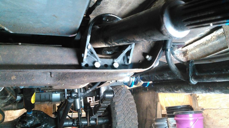 Underside of a vehicle showing driveshaft support bracket, leaf springs, and tire.