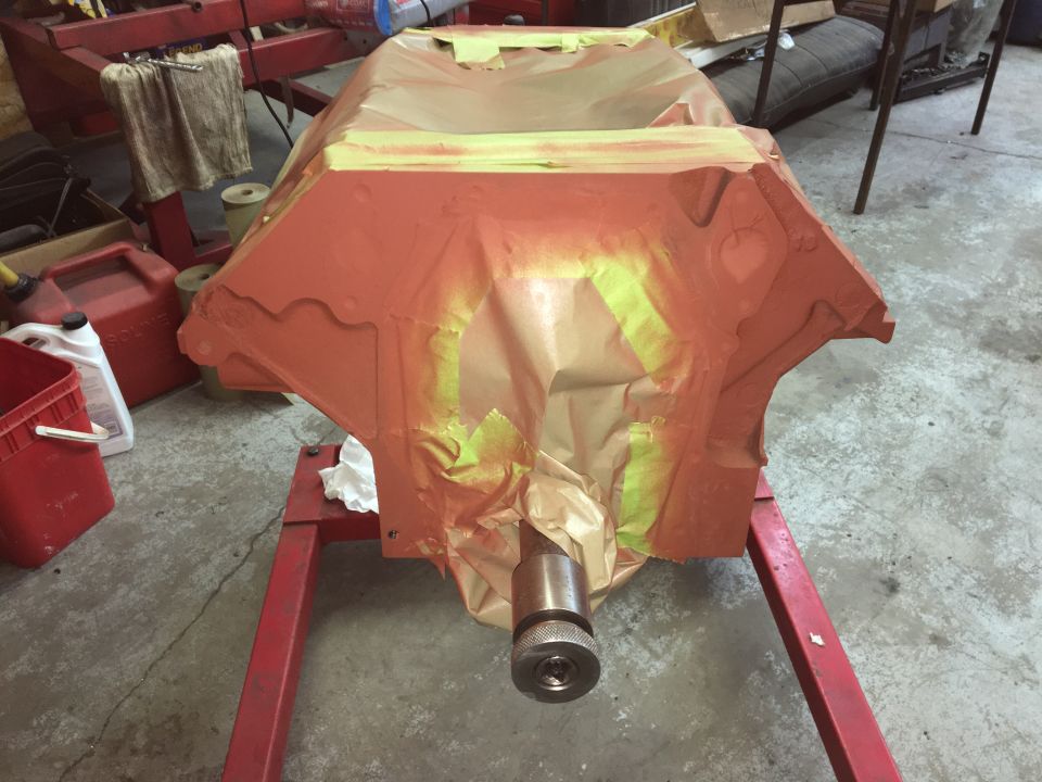 Orange engine block covered in masking paper and tape on a red engine stand.