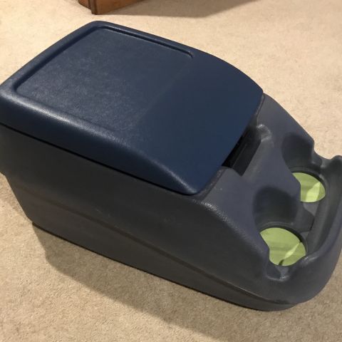 1995 Ford Bronco - A dark gray and blue plastic center console with two cup holders is shown resting on a carpeted surface. The console has a hinged lid that…