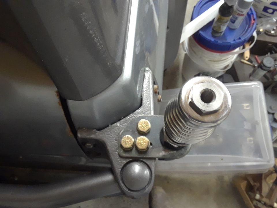 Close-up of a vehicle's rear suspension part with a threaded shock absorber and gold bolts.