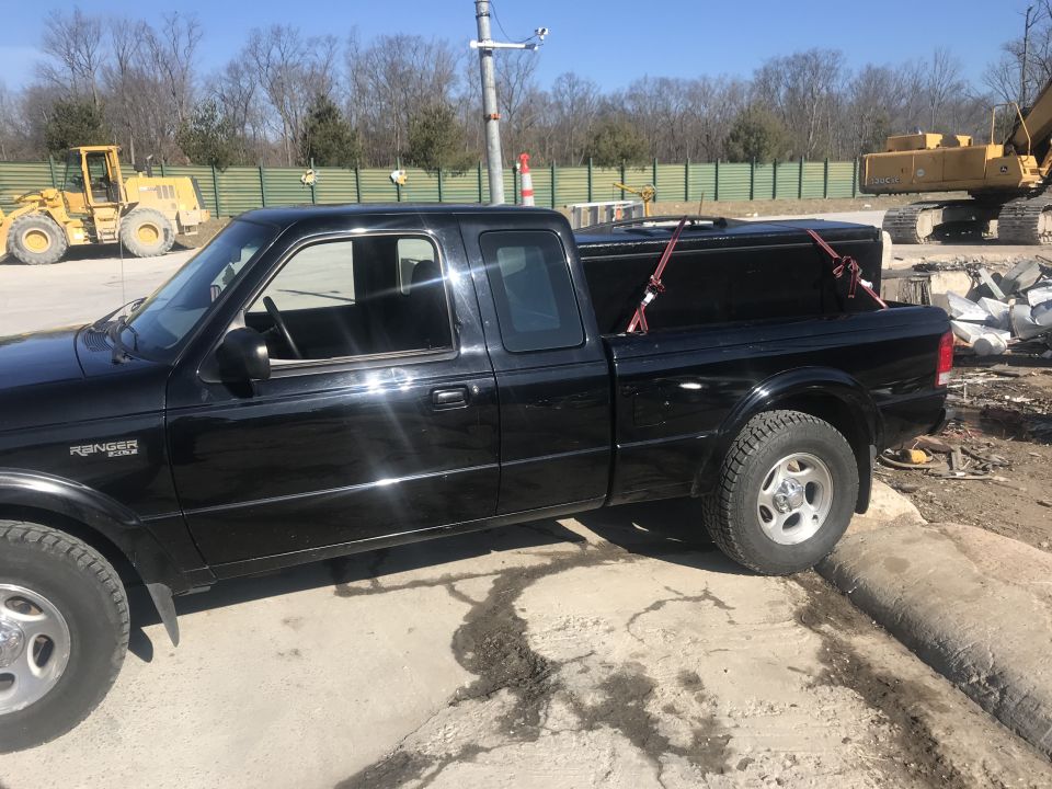Black Ford Ranger pickup truck with a tonneau cover at a construction site.