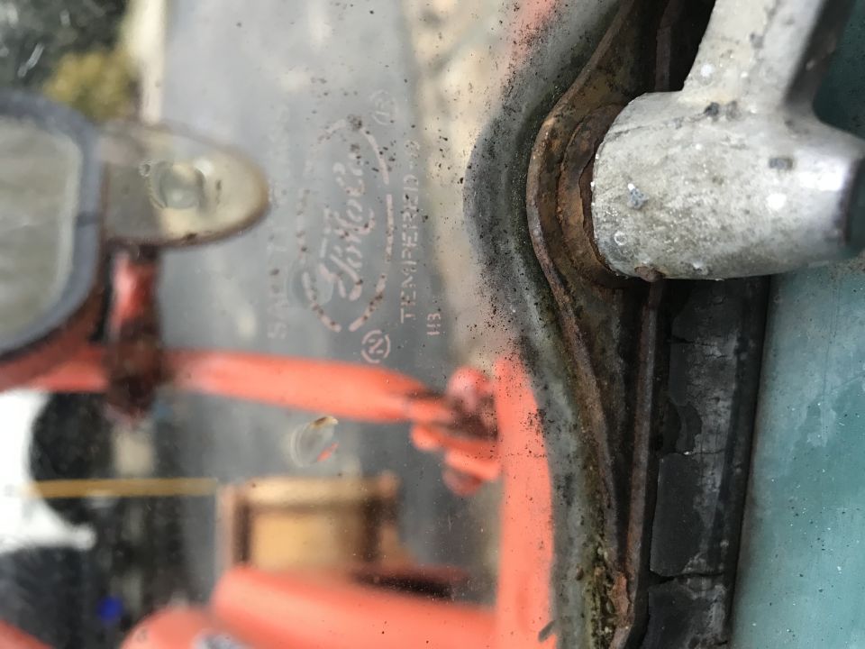 Close-up of vintage Ford tempered glass windshield with markings and rusty frame.
