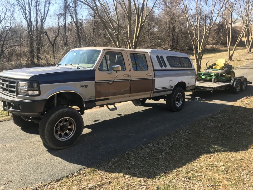 Lifted Ford pickup truck towing a trailer with a lawnmower.