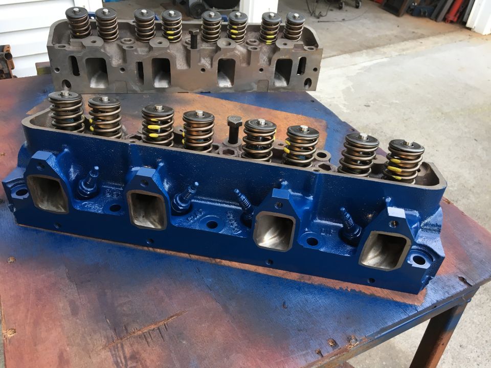 Two Ford V8 engine cylinder heads, one blue, one unpainted, with valve springs visible.