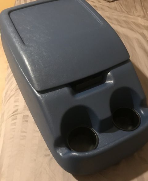 1995 Ford Bronco - A blue plastic center console with two cup holders is shown from a high angle, resting on a striped fabric surface.