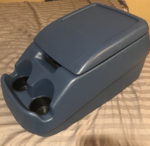 1995 Ford Bronco - A blue plastic center console with two cup holders is shown in a close-up, angled shot. The console has a hinged lid and a latch mechanism…