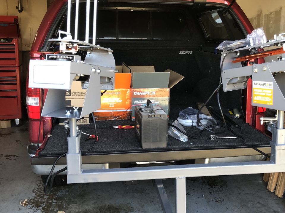 Red pickup truck bed with clay target throwers, boxes, and battery.