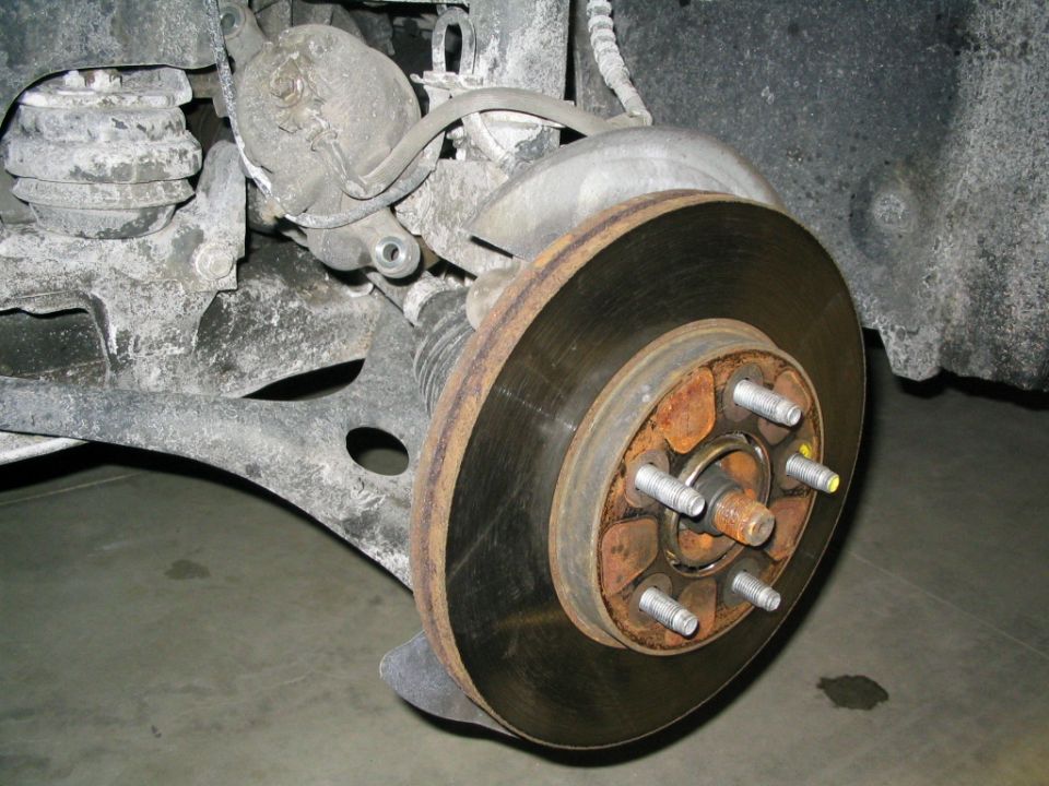 close-up of a rusty car brake rotor, hub, and caliper assembly