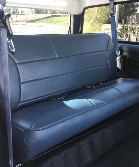 1995 Ford Bronco - The interior of a vehicle shows a blue vinyl bench seat with seat belts. The seat is viewed from the side, with a window in the background…