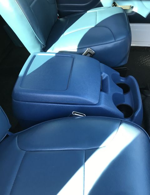 1995 Ford Bronco - The interior of a vehicle shows blue vinyl seats and a blue center console with cup holders. Sunlight streams across the seats, highlightin…