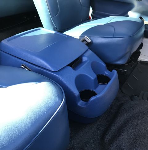 1995 Ford Bronco - The interior of a vehicle shows a blue center console with two cup holders and a storage compartment, flanked by blue vinyl seats. The floo…