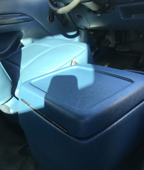 1995 Ford Bronco - The interior of a vehicle shows a blue vinyl bench seat and a blue center console with a hinged lid. Sunlight streams in from the side, cas…