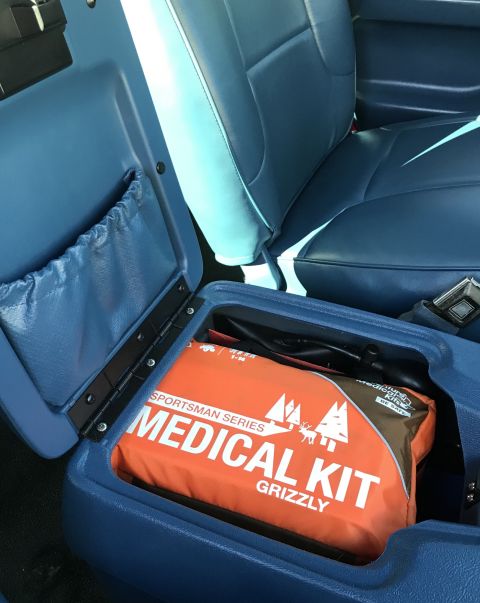 1995 Ford Bronco - An open blue center console in a vehicle reveals an orange medical kit bag labeled "SPORTSMAN SERIES MEDICAL KIT GRIZZLY". A blue fabric po…