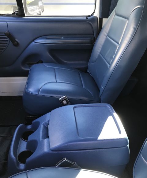 1995 Ford Bronco - The interior of a blue vehicle shows a driver's seat, door panel, and a center console with cup holders. A seatbelt buckle is visible on th…