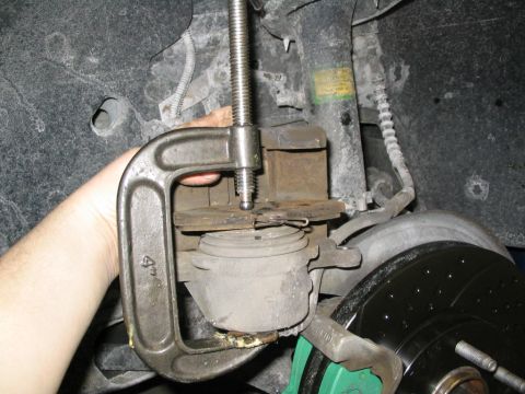 1996 Mercury Sable - A C-clamp is used to compress a brake caliper, revealing a green caliper bracket and a drilled brake rotor.